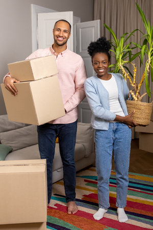 Couple holding cardboard box after moving in new apartment standing in living room