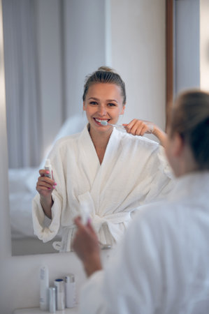 Young woman in white robe cleaning teethの写真素材