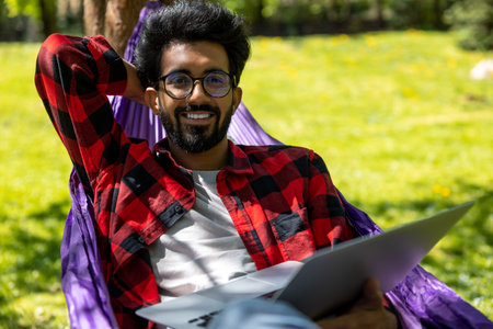 Young hindu man laying in hammock and working on laptop