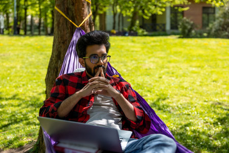 Young hindu man laying in hammock and working on laptop