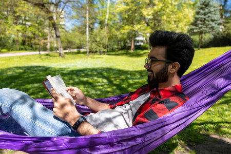 Contented young man in hammock reading a bookの写真素材