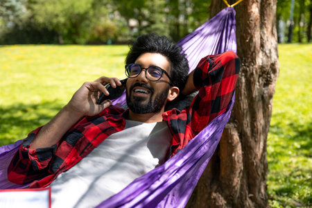 Contented hindu young man talking on the phone and laying in hammock