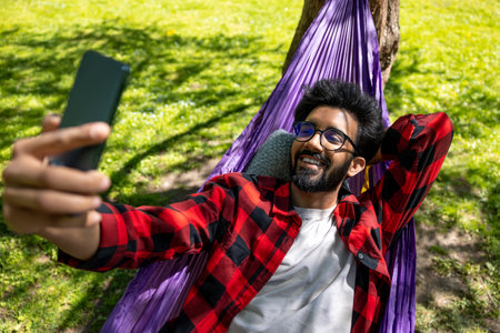 Smiling hindu man making selfie while laying in hammock