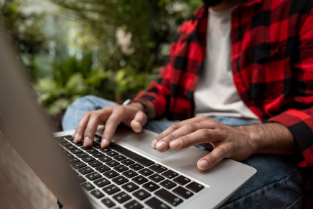 Man in red checkered shirt working on laptop in a garden