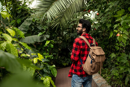 Dark-haired hindu man with backpack walking in botanical garden