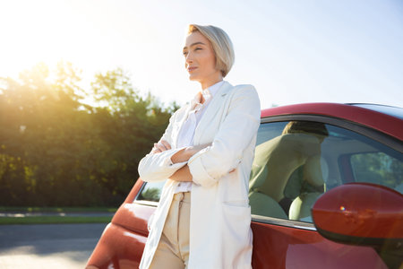 Beautiful adult woman standing near her new red carの写真素材