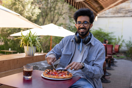 Man sitting at the table in a cafe cutting pizza