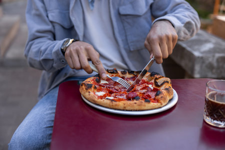 Man sitting at the table in a cafe cutting pizzaの写真素材