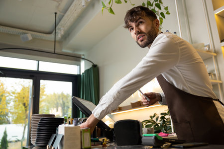 Male barista at counter using cashbox computer in cafe store checking clients order