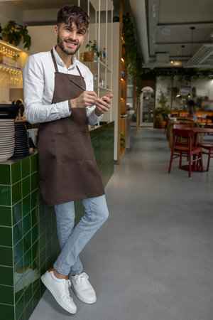 Barista with beard standing in bar counter and using organizer for counting stock in restaurantの写真素材