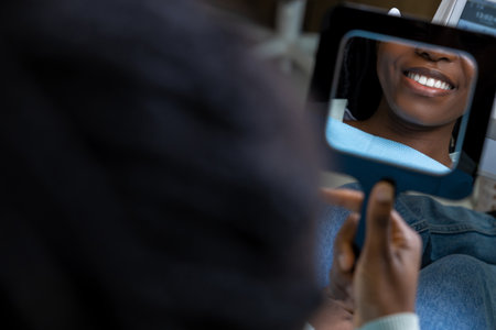 Cheerful multicultural woman patient looking at mirror after dental treatment