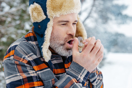 Mature man in warm hat warming his hands with his breathの写真素材
