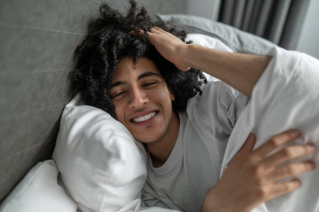 Young brunette man lying in bed and looking sleepyの写真素材