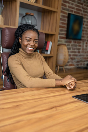 Happy satisfied multicultural woman sitting at table in office interiorの写真素材
