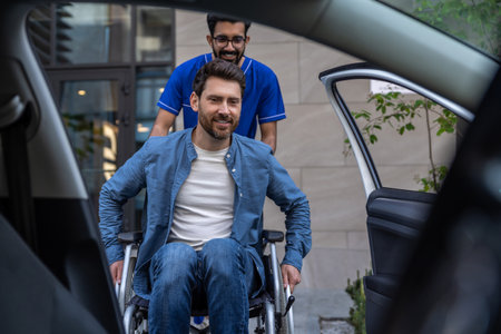 Disabled man getting on a car, male nurse helping himの写真素材