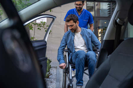 Disabled man getting on a car, male nurse helping himの写真素材