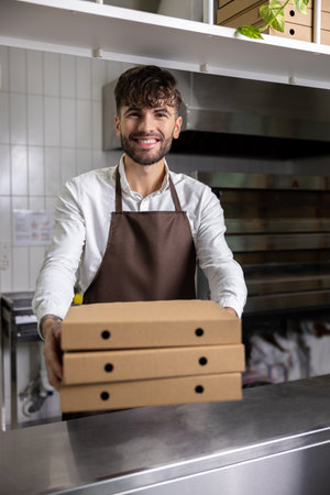 Man holding pizza boxes works in restaurant kitchen preparing tasty meals for delivery and takeaway