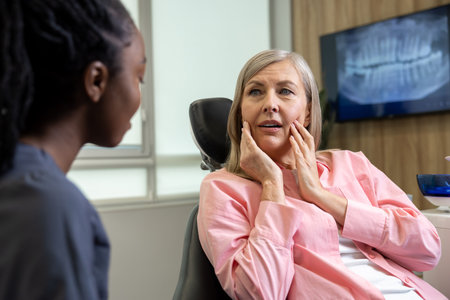 Dentist woman having conversation with blonde middle aged female patient sitting at dental chair