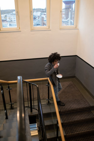Curly-haired young man in eyeglasses at the stairs with a cup in handsの写真素材