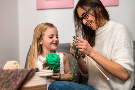 Young woman knitting with her daughter in cozy living room at home