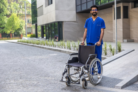 Positive male nurse in blue doctors overall carrying a wheelchairの写真素材