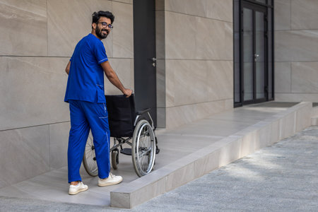 Tall dark-haired man in hospitals yard carrying a wheelchairの写真素材