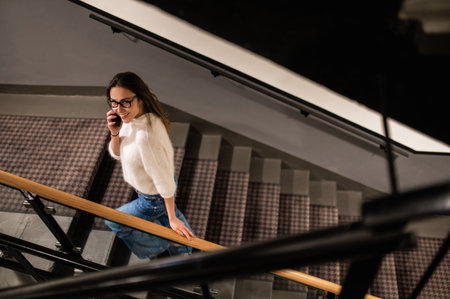 Woman in glasses talking on mobile phone while walking on stairs in hotel