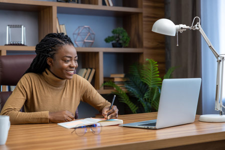 Happy smiling woman sitting at workplace with laptop writing in her organizer