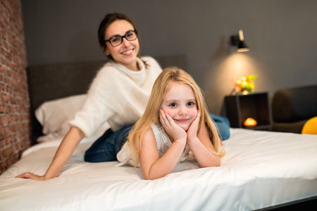 Mother and child girl in bedroom cuddling on cozy warm comfortable bed in hotel roomの写真素材