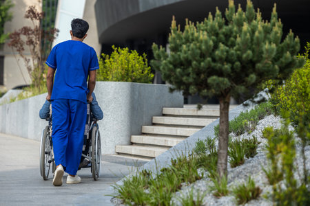 Male nurse in a blue doctors overall carrying a wheelchair