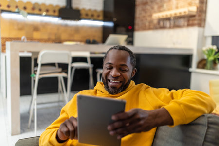 African american man in yellow hoodie with tablet in handsの写真素材