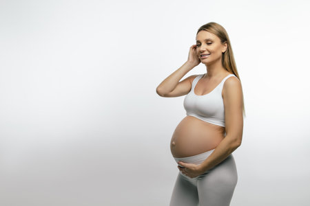 Blonde pregnant woman in white clothes looking thoughtful