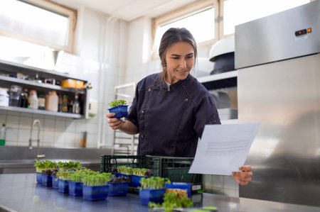 Woman in uniform holding microgreens in restaurant kitchen