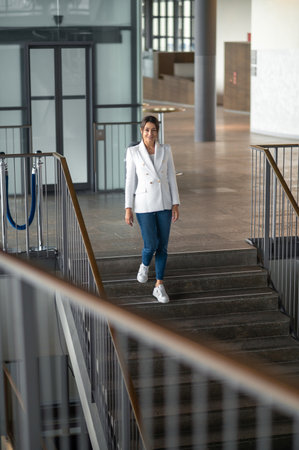 Woman in white jacket and jeans on the stairs in the office building