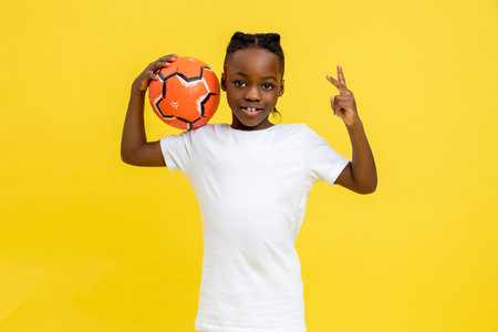 Little African American joyful boy playing football on kids championship showing v sign