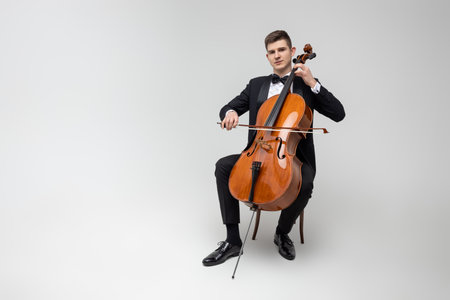 Passionate cello player sitting on chair performing concert isolated over white background
