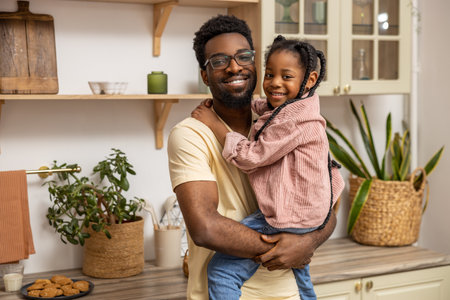 Smiling black man holding his little daughter in kitchen interior