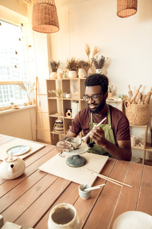 Smiling man painting pottery and looking enjoyed