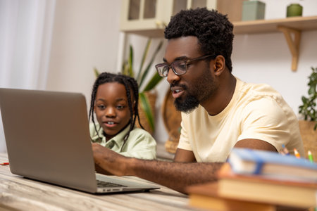Black man with his daughter using laptop together while doing homework