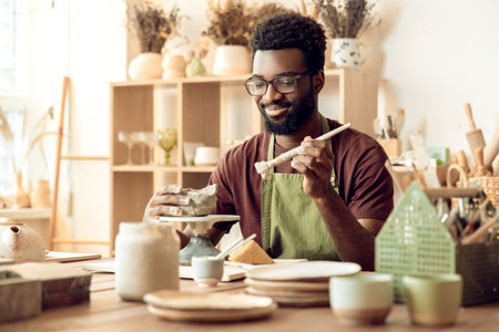 Dark-skinned bearded painting pottery and looking contentedの写真素材