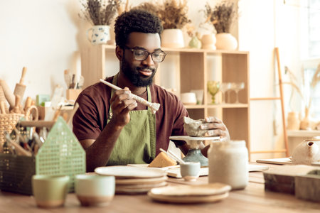 Dark-skinned bearded painting pottery and looking contentedの写真素材