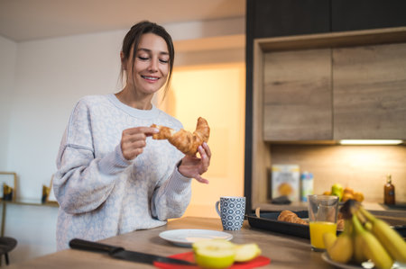 Cute young woman having croissants for breakfast and looking enjoyedの写真素材