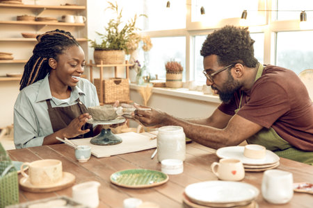 Cute dark-skinned woman having a pottery master class with a male sculptorの写真素材