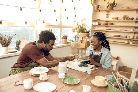 Cute dark-skinned woman having a pottery master class with a male sculptorの写真素材
