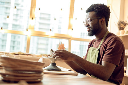 Curly-haired man sitting at the table, working with clay and looking involved