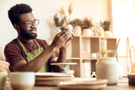 Dark-skinned man at the table with piece of clay in hands