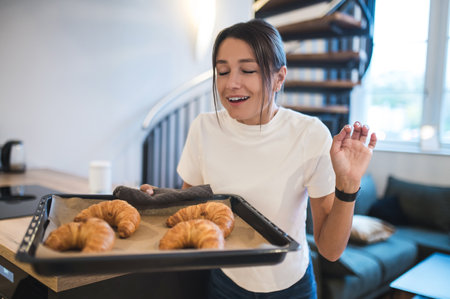 Dark-haired woman with a tray of fresh homemade croissants looking happy
