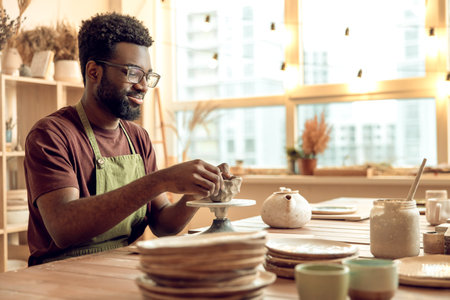 Curly-haired man sitting at the table, working with clay and looking involved