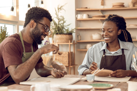 African american male sculptor explaining something to a female student in a pottery workshop