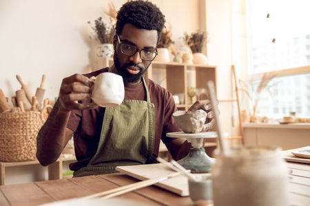 Dark-skinned sculptor working in his workshop and looking involved